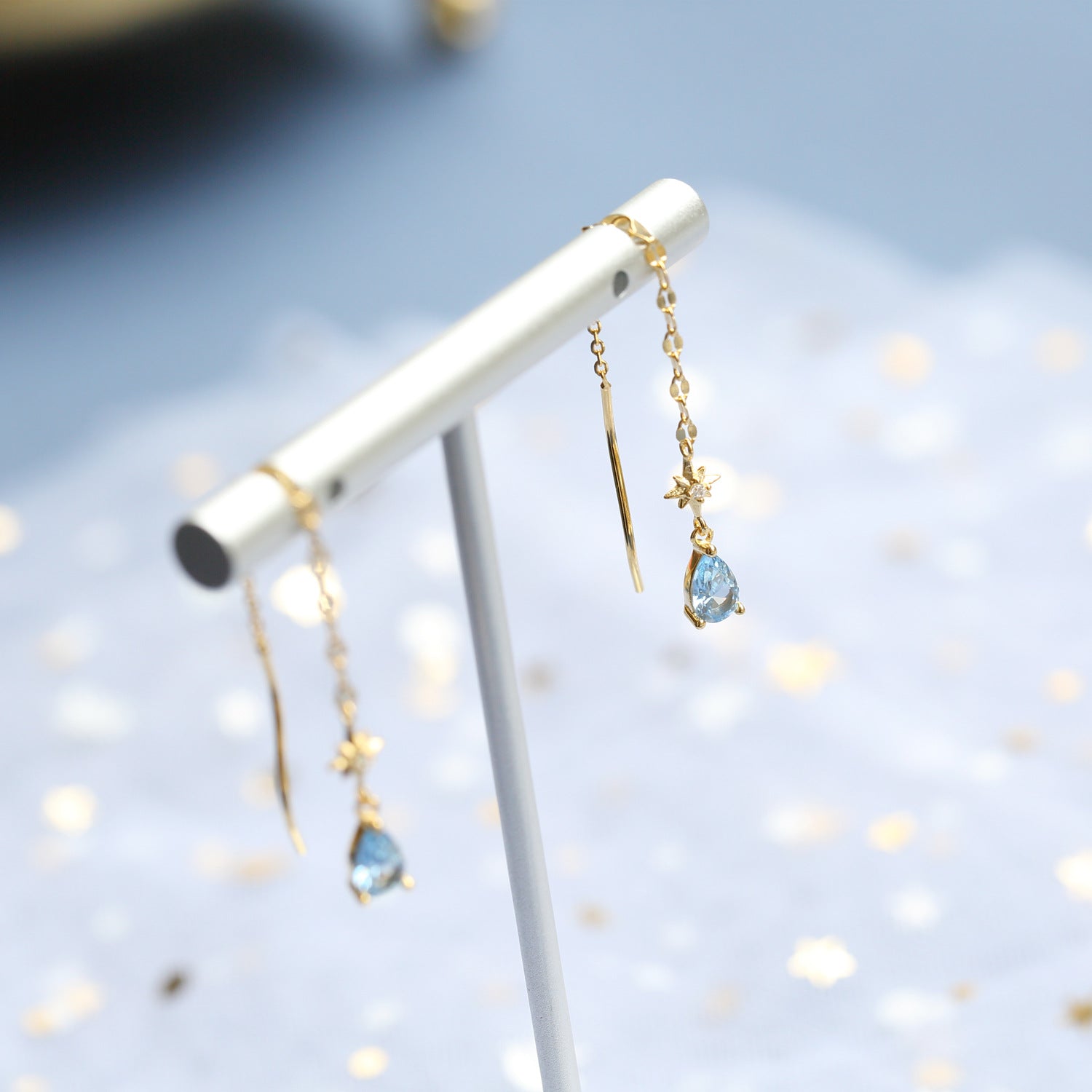 Gold earrings with blue gemstones on a white stand from Gembee Jewellery