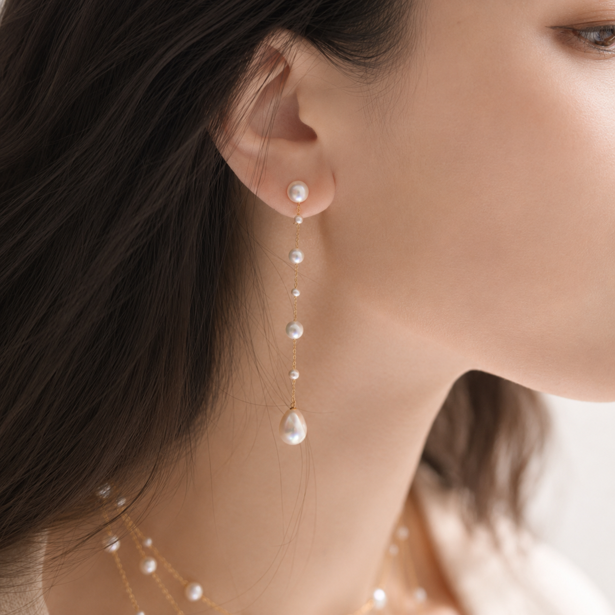 Gold chain pearl drop earrings with graduated freshwater pearls, worn close-up on model's ear