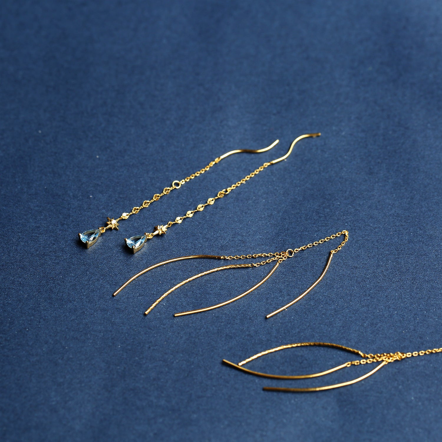 Gold earrings with blue gemstones on a blue background from Gembee Jewellery