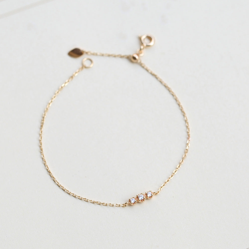 Gold bracelet with small stones on a light gray background from the GemBee Jewellery.
