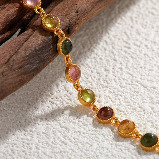 Gold bracelet with multicoloured tourmaline beads  on a textured surface