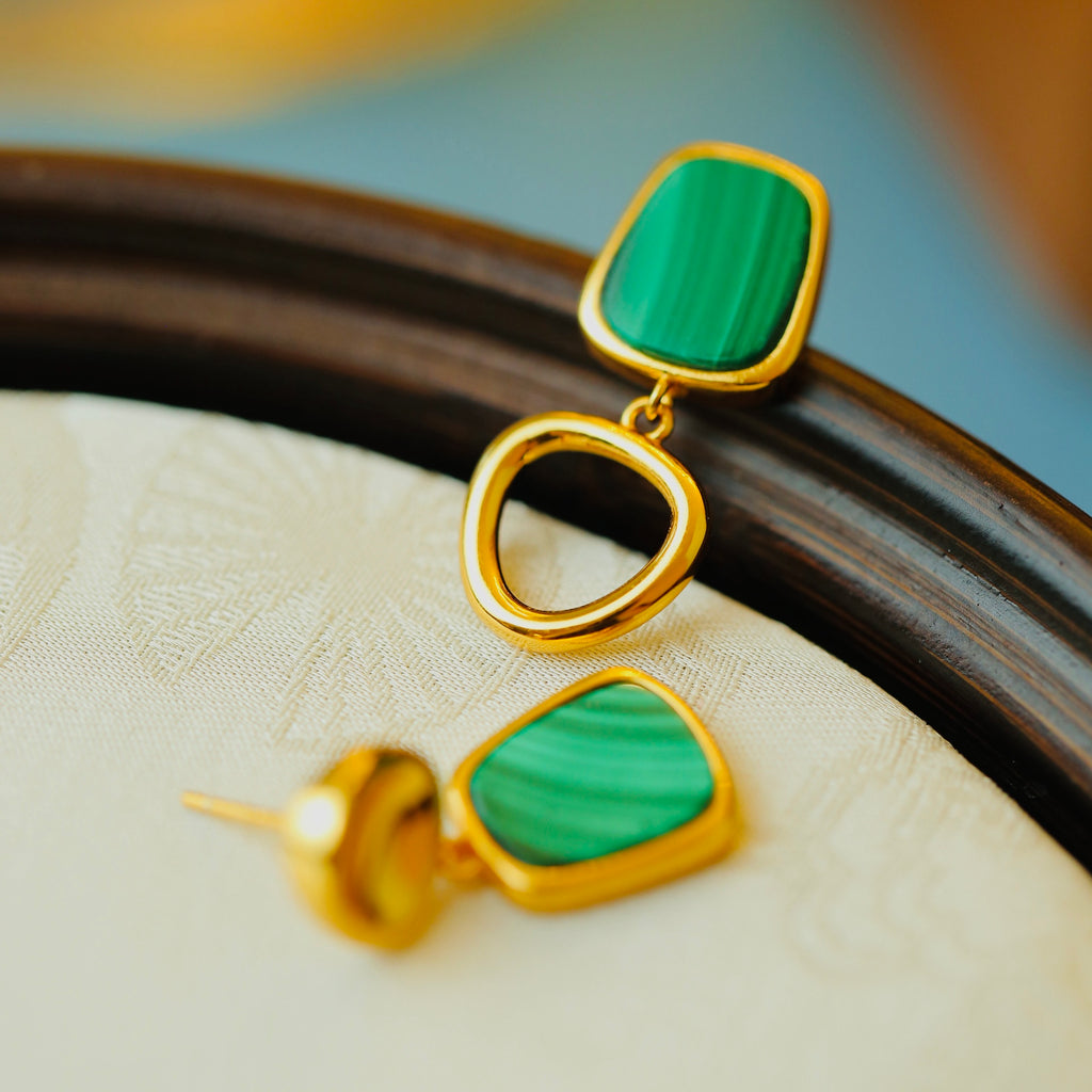 Gold earrings with green stones on a textured surface