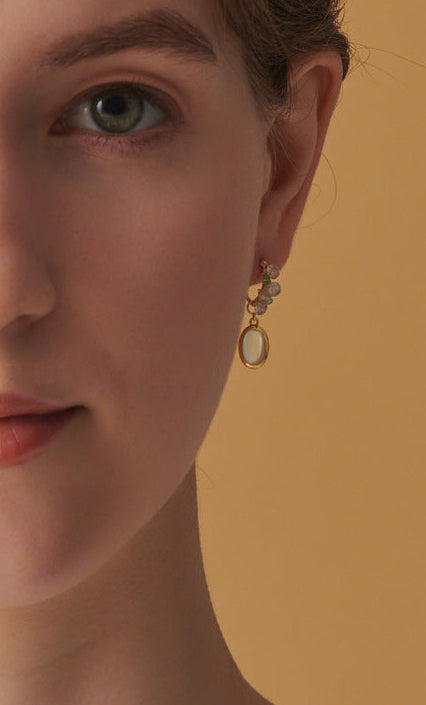 Close-up of a woman wearing gold earrings against a beige background