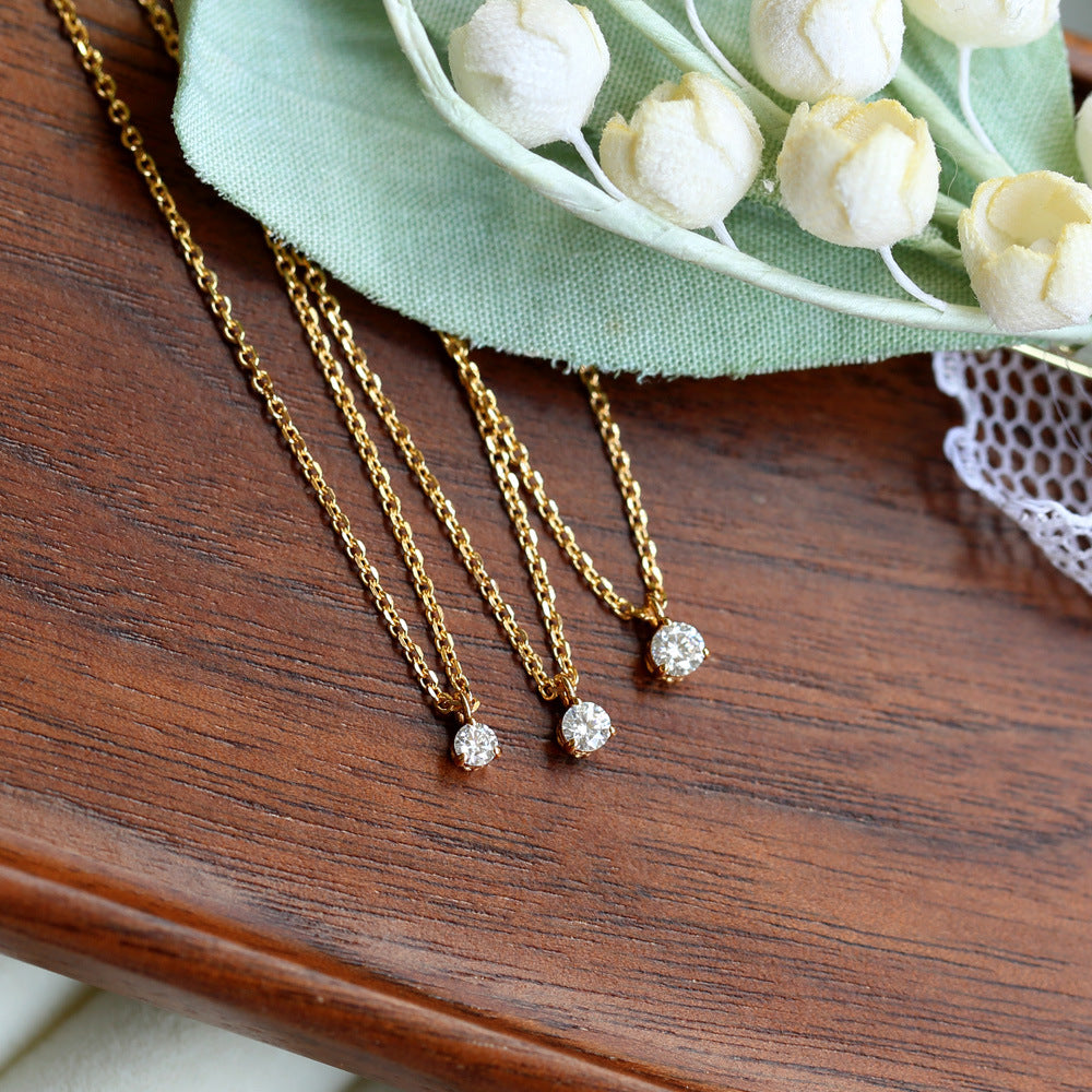Two gold necklaces with diamond pendants on a wooden surface with white flowers in the background.