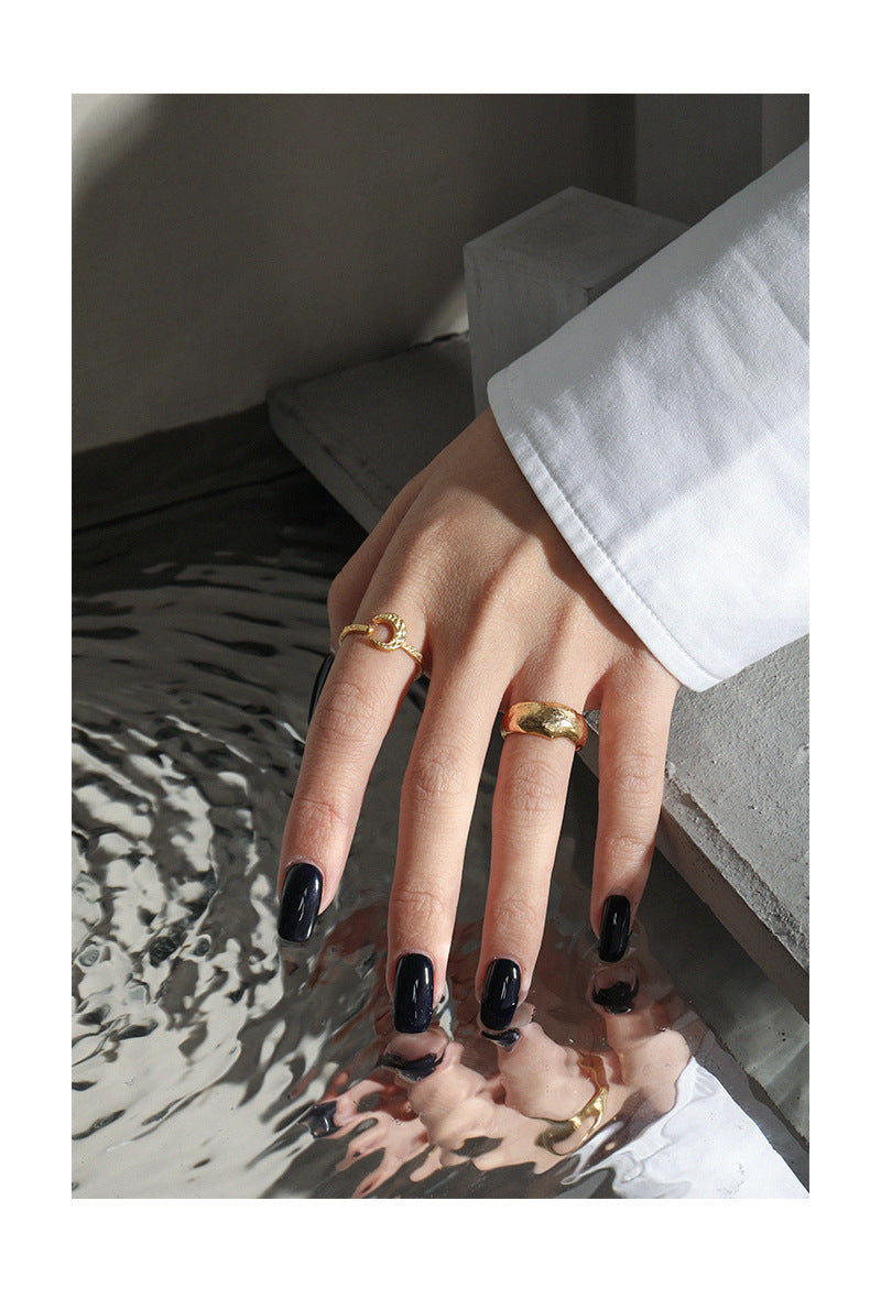 Hand with black nail polish and gold rings on a textured surface