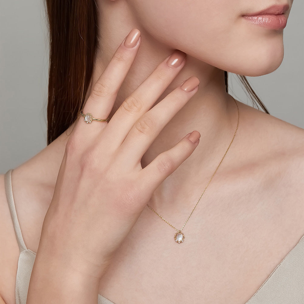Close-up of a woman wearing a gold necklace and ring on a neutral background