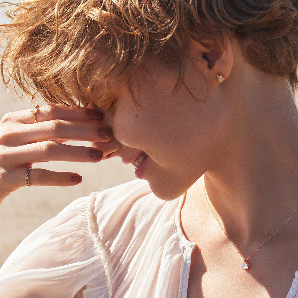 Close-up of a person with short hair wearing earrings and a necklace, with a blurred background.