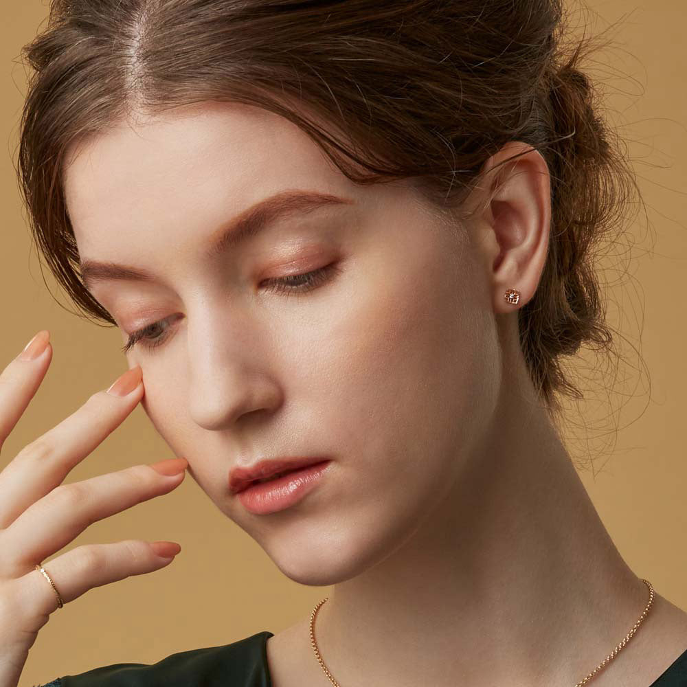 Close-up of a woman wearing a gold earring and necklace against a beige background