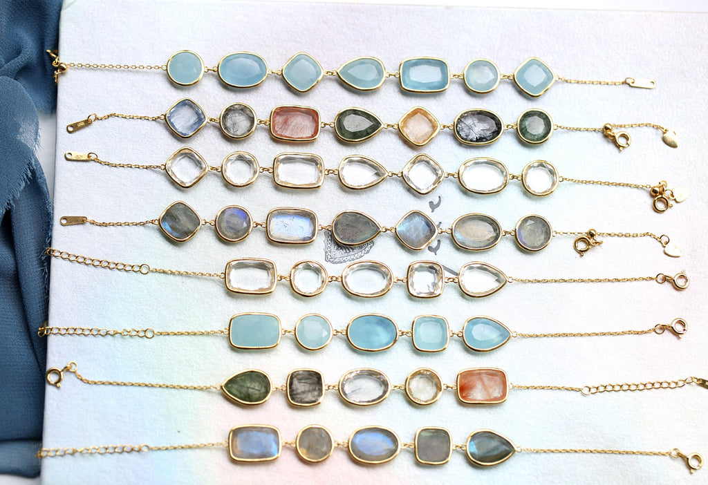 Collection of gold bracelets with various gemstones on a white surface