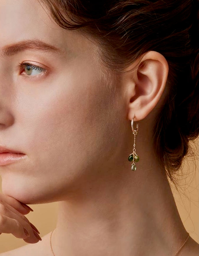Close-up of a person wearing a delicate earring with green stones on a neutral background