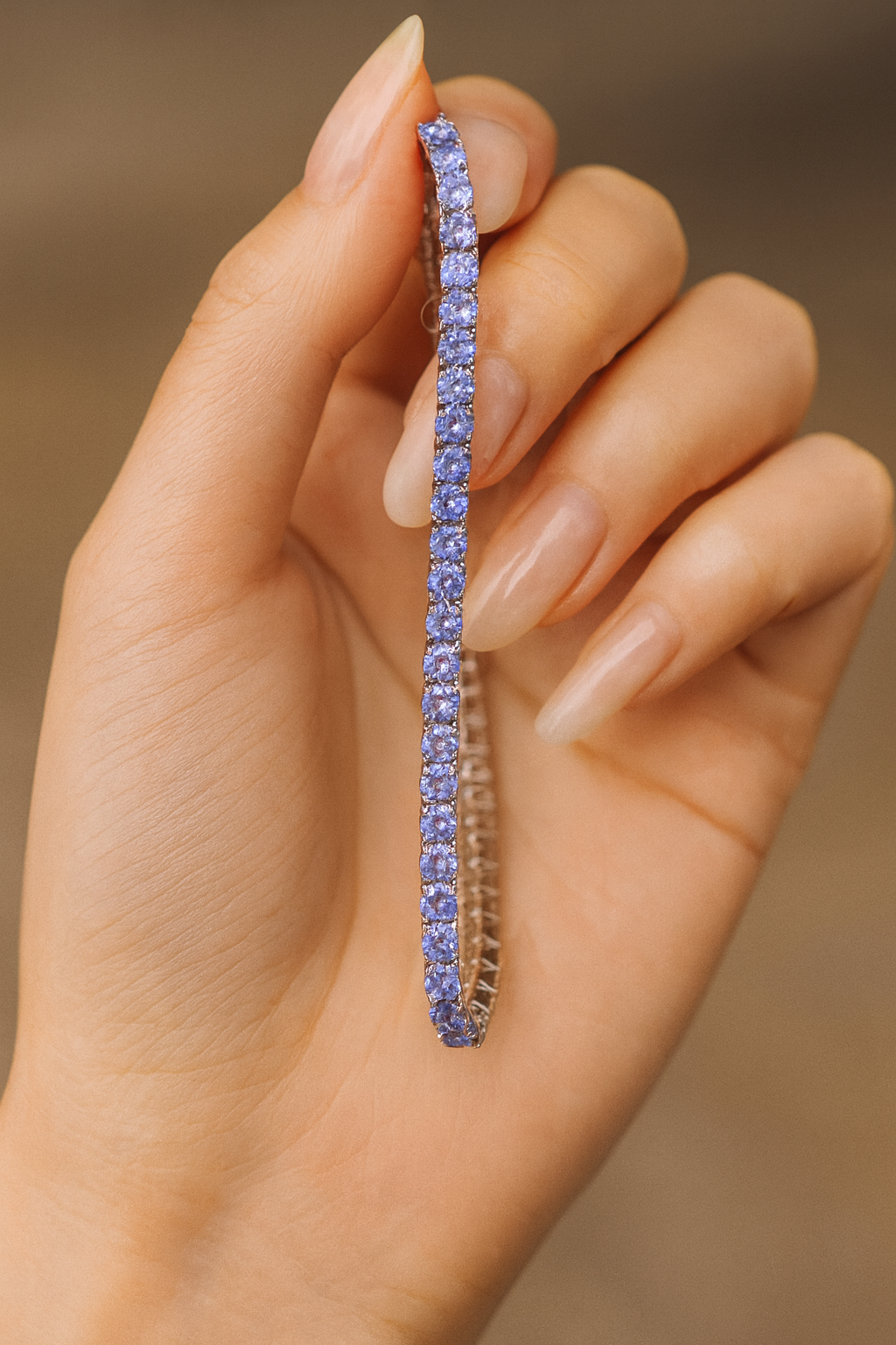 Hand holding a blue gemstone tanzanite tennis bracelet against a neutral background